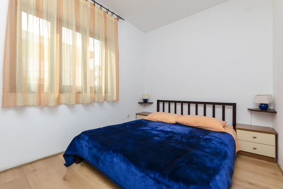A bedroom with a bed, a nightstand, a lamp, and sheer curtains.