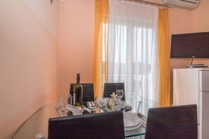 Ein Essbereich mit einem für zwei gedecktem Tisch, einer Weinflasche und einem an der Wand befestigten Fernseher.