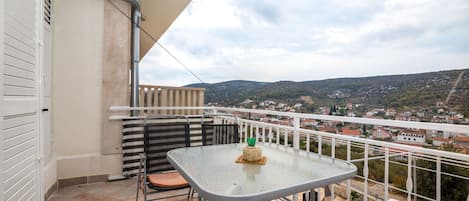 Un balcón con mesa y sillas, y una vista de un pueblo y colinas al fondo.