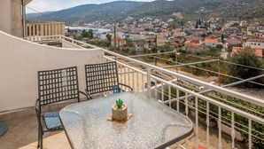 A balcony with a table and chairs, overlooking a town and hills. - Apartments Mirjana (Marina)