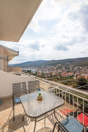 Un balcon avec une table et des chaises, un pot de fleurs et une vue sur une ville et des collines.