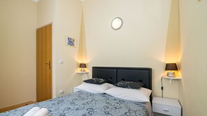 A neatly made bed with patterned bedding, two bedside lamps, a small bedside table, and a door to the left. - Apartments Mirjana (Marina)