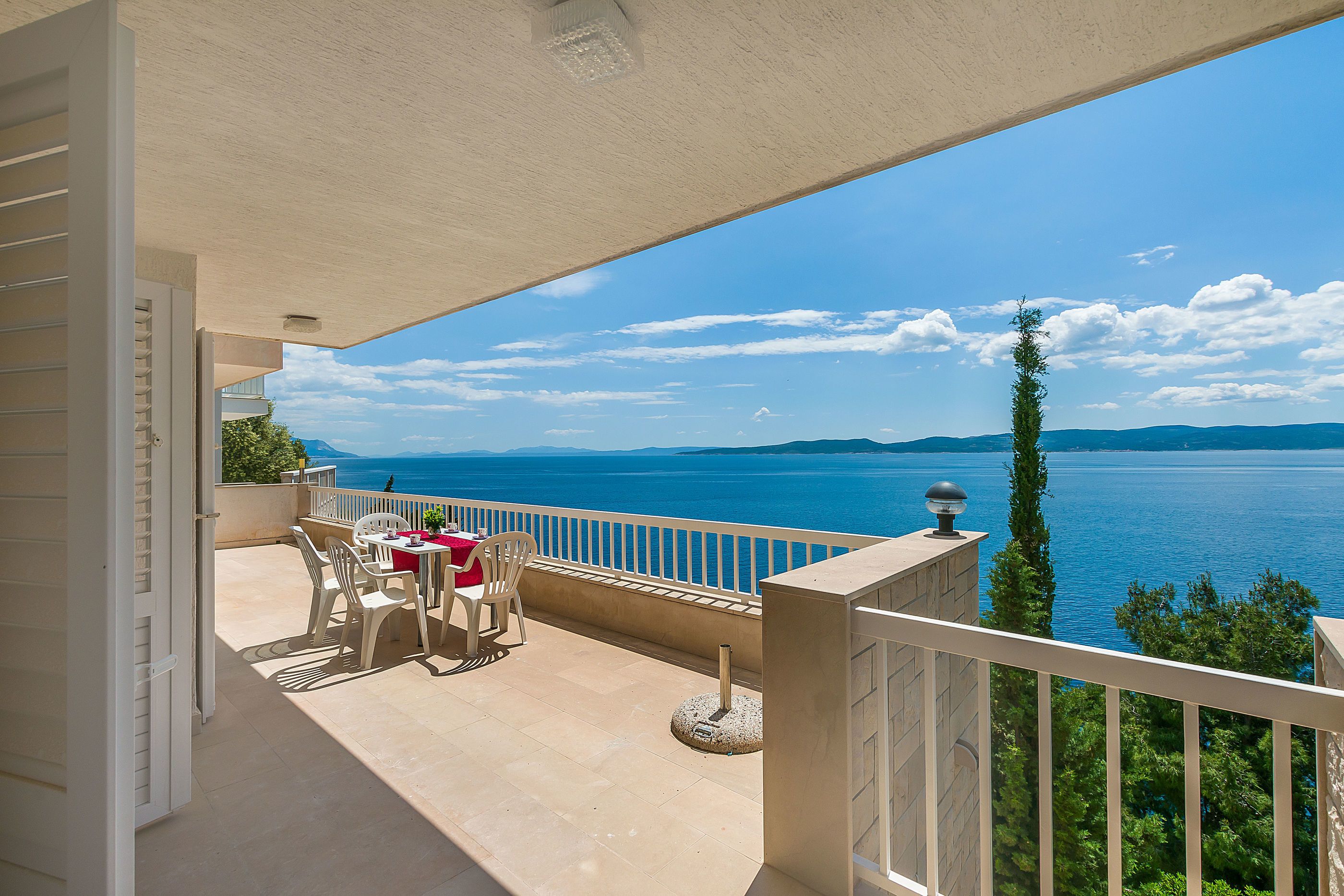 A balcony with a table and chairs, overlooking a body of water and distant mountains.