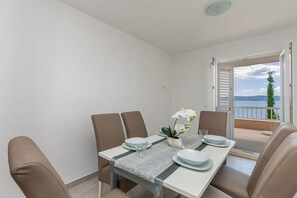 Zona pranzo con tavolo apparecchiato per quattro persone, un'orchidea in vaso e vista sul mare attraverso porte aperte.