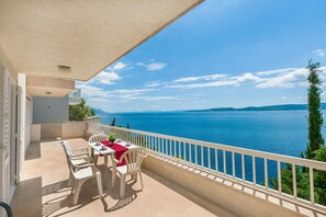 Un balcon avec une table et des chaises, donnant sur une vaste étendue d’eau et sur des montagnes lointaines.