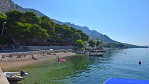 A beach with clear water, people sunbathing, and boats. - Apartment and Rooms Tatijana (Omis)