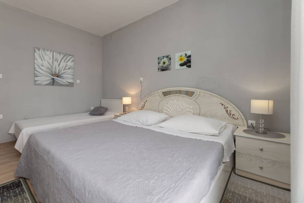 Une chambre à coucher avec un lit double, deux tables de chevet avec des lampes, une tête de lit ornée de motifs floraux et deux tableaux représentant des fleurs, accrochés au mur.