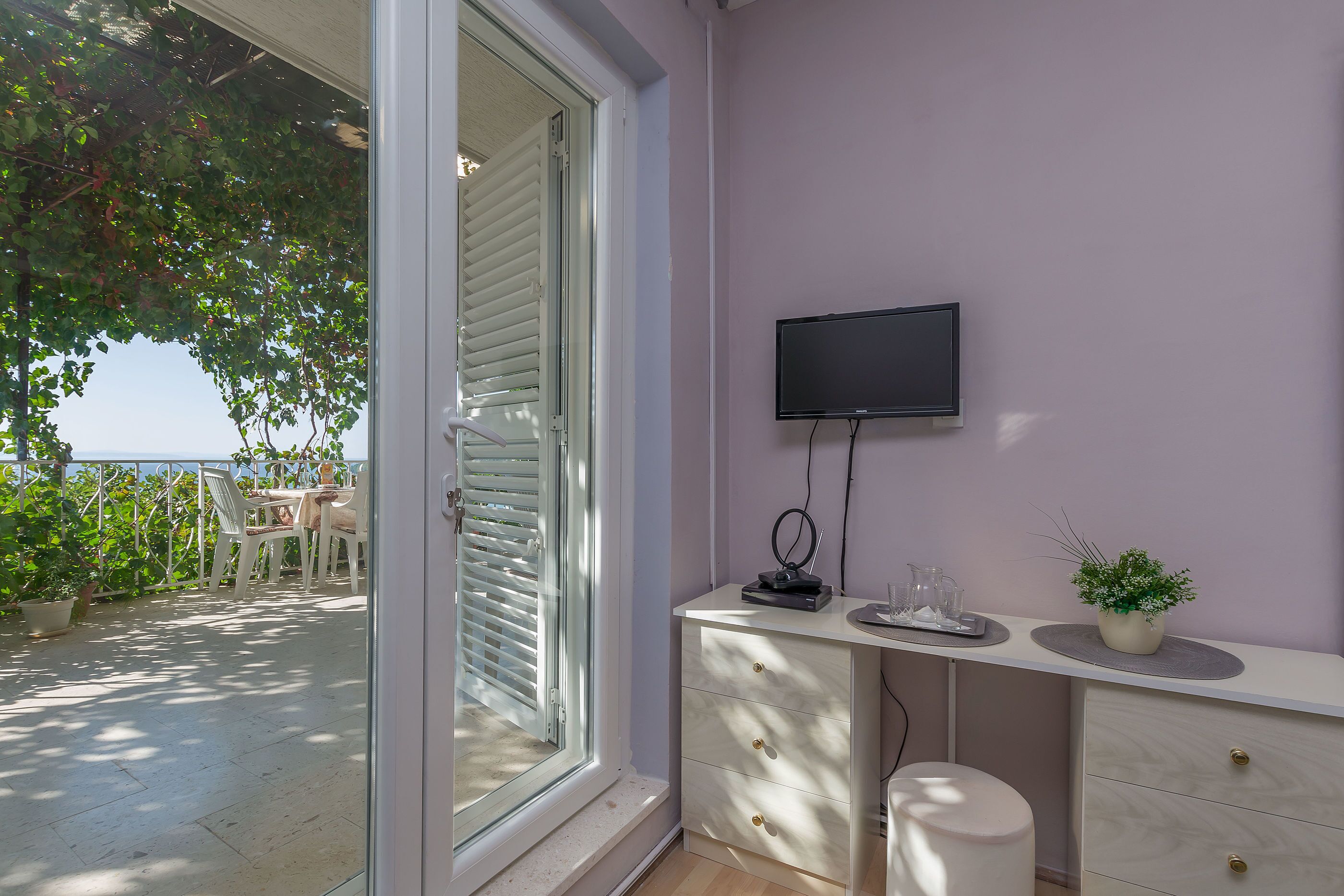 Ein Balkon mit Tisch und Stühlen, ein an der Wand montierter Fernseher und ein Blumentopf.