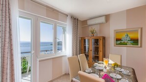 A dining area with a table set for four, a cabinet with glass doors, and a painting on the wall. - Apartment and Rooms Tatijana (Omis)