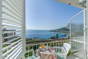 Enjoy breathtaking views of the sea and coastal town from this balcony, featuring a table for two and comfortable seating.