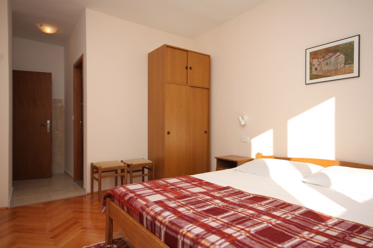 A bedroom with a bed, a wooden wardrobe, a small table, and a chair.