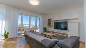 Una sala moderna con un sofá grande de color gris, un televisor de pantalla plana montado en la pared y una mesa de comedor con sillas.