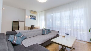 Una sala de estar moderna con un sofá gris, una mesita blanca y un ventanal con cortinas traslúcidas.