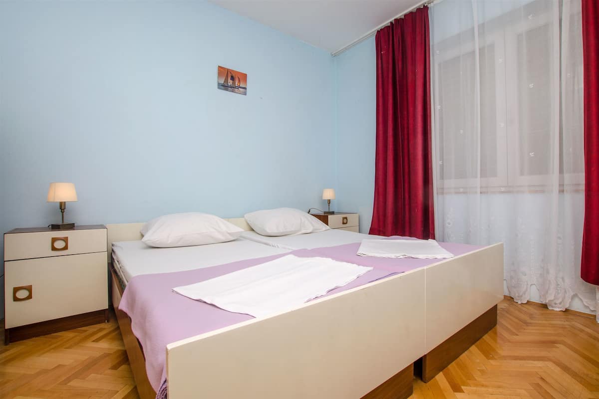 Une chambre à coucher comprenant un lit, deux tables de chevet, une commode, une fenêtre avec des rideaux et un tableau accroché au mur.