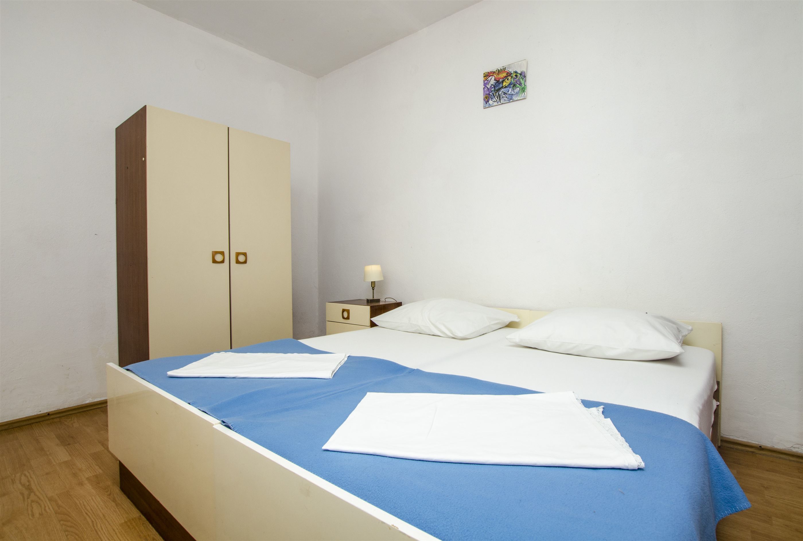 A bedroom with a bed, a wardrobe, a nightstand, and a wall-mounted artwork.