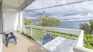 En balkon med et bord og stole, der giver udsigt over et smukt hav- og bjerglandskab.
