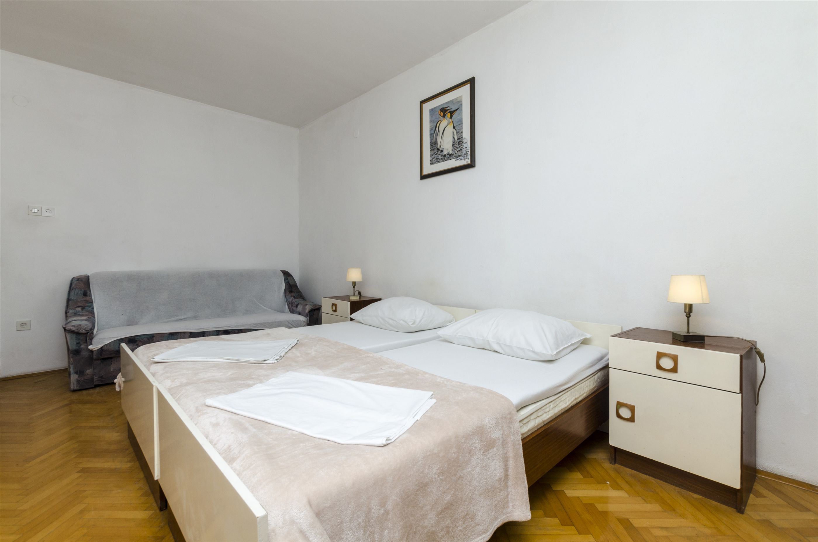 A bedroom with two beds, a nightstand with a lamp, a framed picture on the wall, and a couch.