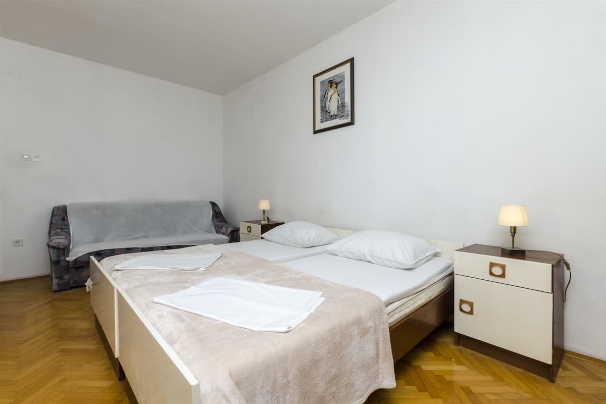 Une chambre avec deux lits, une table de chevet avec une lampe, un tableau encadré au mur et un canapé.