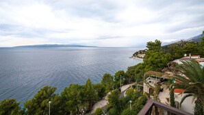 A coastal property with a view of the sea, surrounded by greenery and a stone building. - Apartments Igor (Bratus)