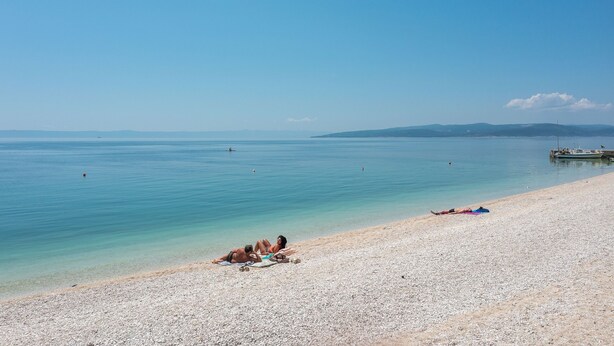 A pebbled beach with clear blue water and distant mountains. - Apartments Igor (Bratus)