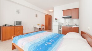 A bedroom with a bed, a desk, a chair, a television, and a kitchenette. - Apartments Igor (Bratus)