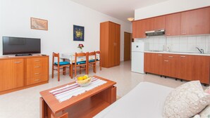 A compact living space with a kitchenette, a dining area with a table and chairs, a television, and a small decorative vase. - Apartments Igor (Bratus)