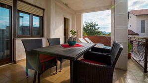 Un balcón con una mesa, sillas, una planta en maceta y vistas de los edificios circundantes.