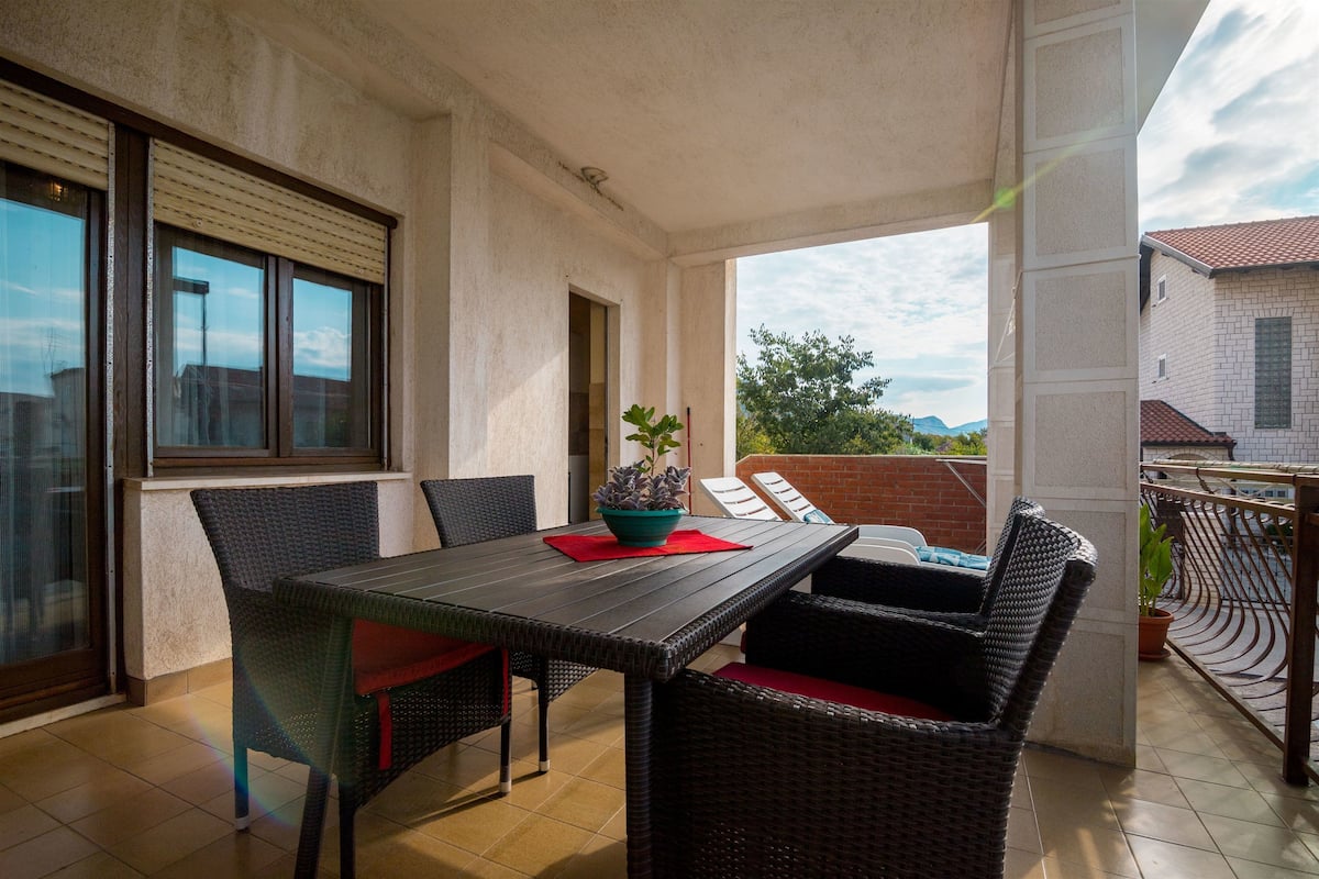 A balcony with a table and chairs, a potted plant, and a view of the surrounding buildings.