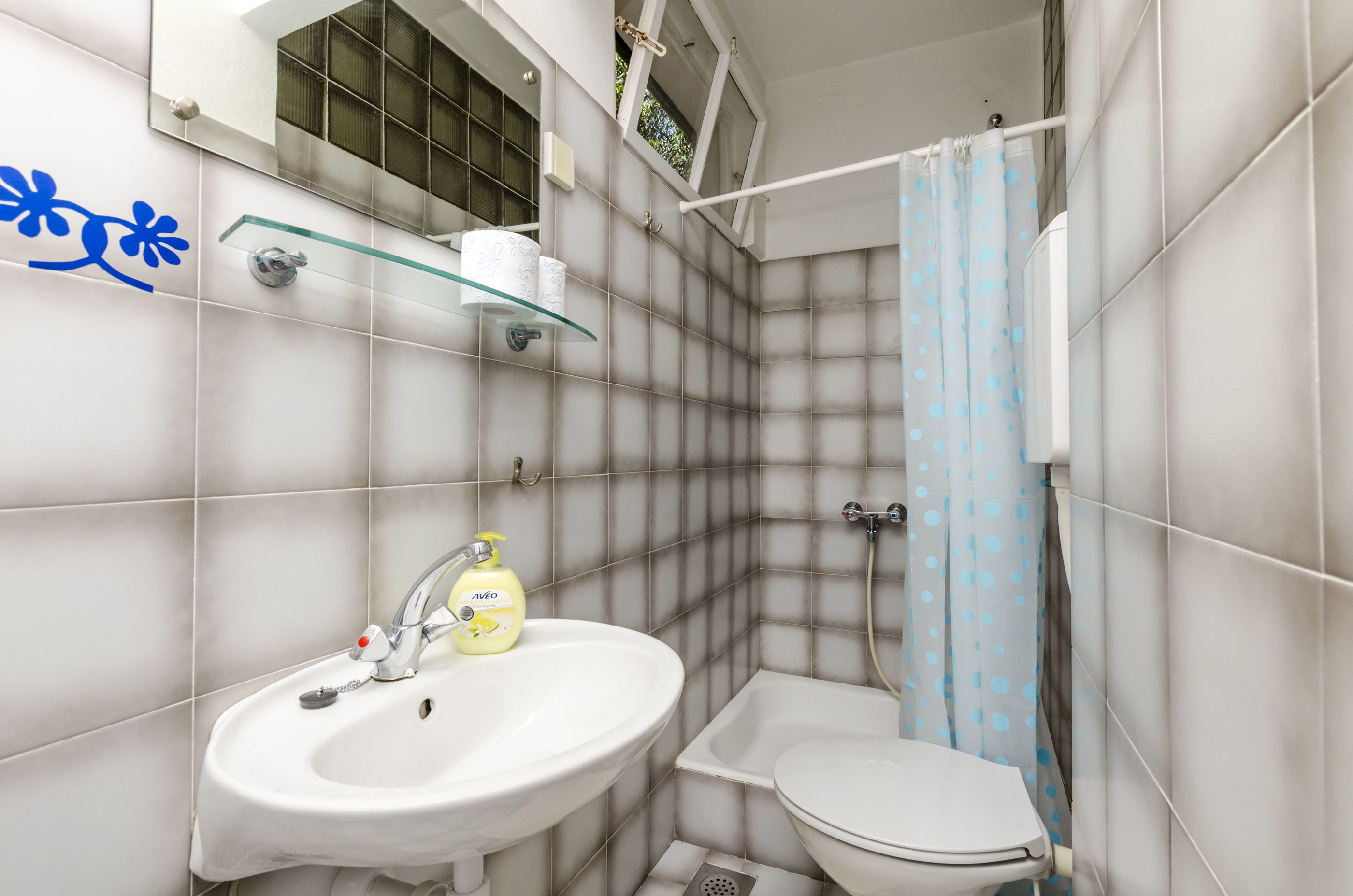 A bathroom with a white sink, toilet, and glass shelf with toiletries.