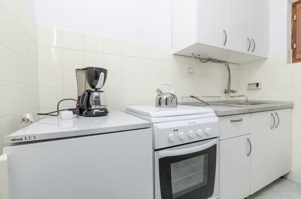 A kitchen with white cabinets, a stove, an oven, a coffee maker, and a kettle.