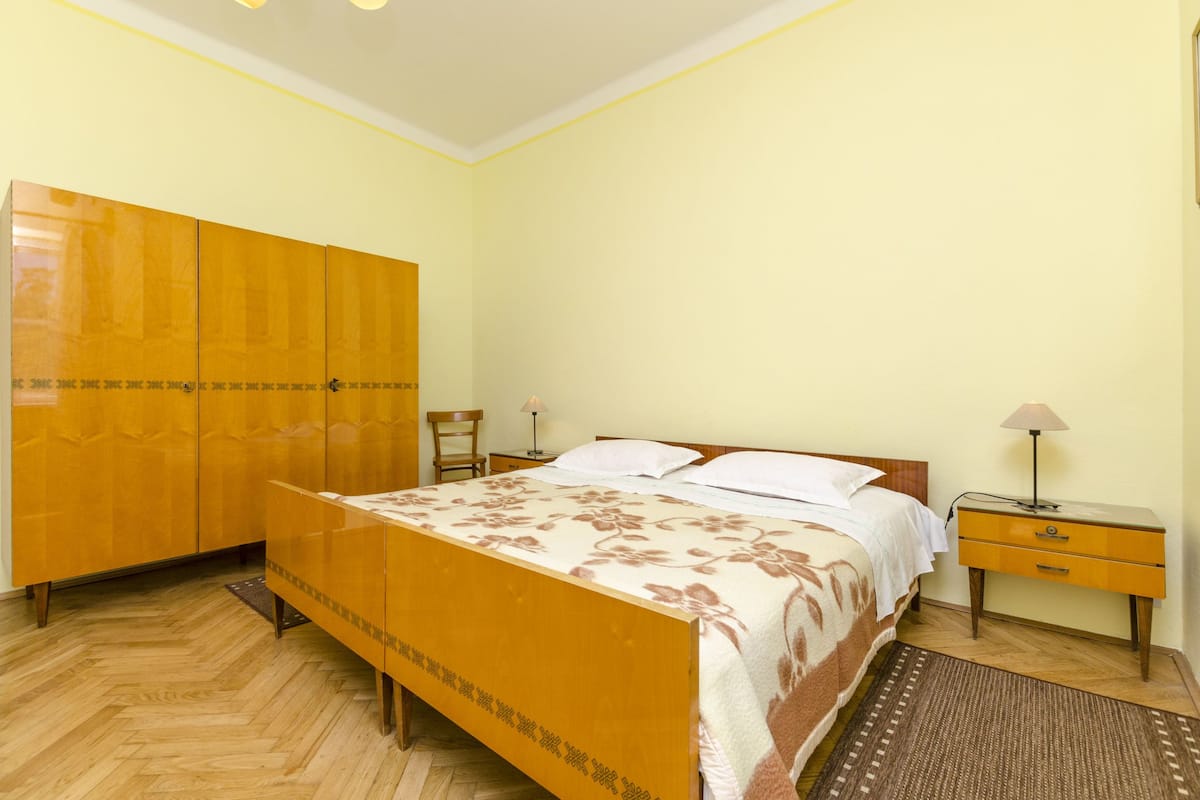 A bedroom with a bed, a wooden wardrobe, a nightstand, and a lamp.