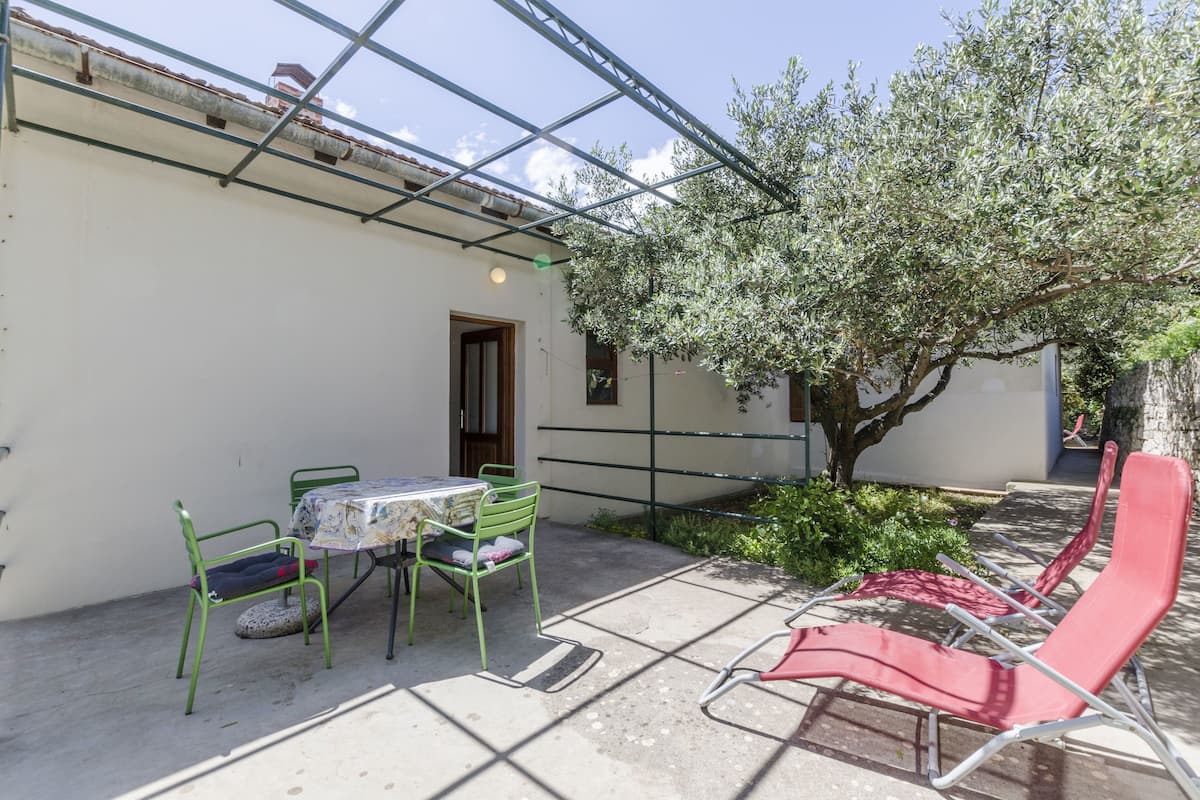 A patio with a table and chairs, a red lounge chair, and a tree.