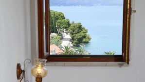 A bedroom with a bed, a window with a view of a lake and mountains, and a wall-mounted lamp. - Apartments Boro (Splitska)