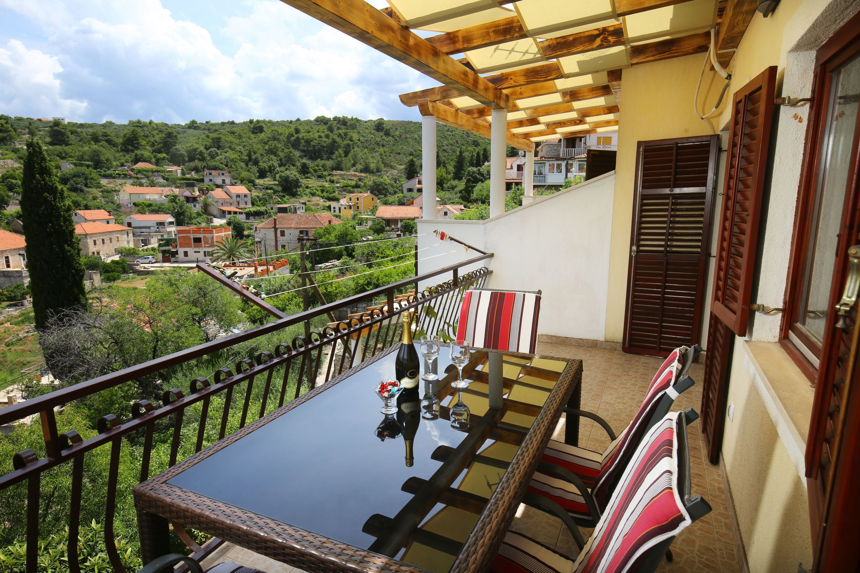 Un balcon avec une table en verre, des chaises en osier et une pergola en bois.