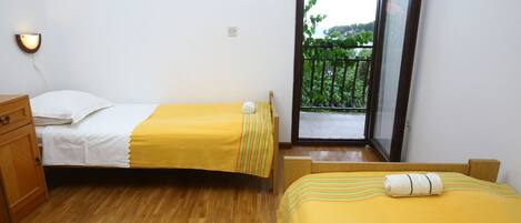 Habitación con dos camas, suelo de madera, un pequeño aparador de madera y un balcón con vistas a la vegetación.