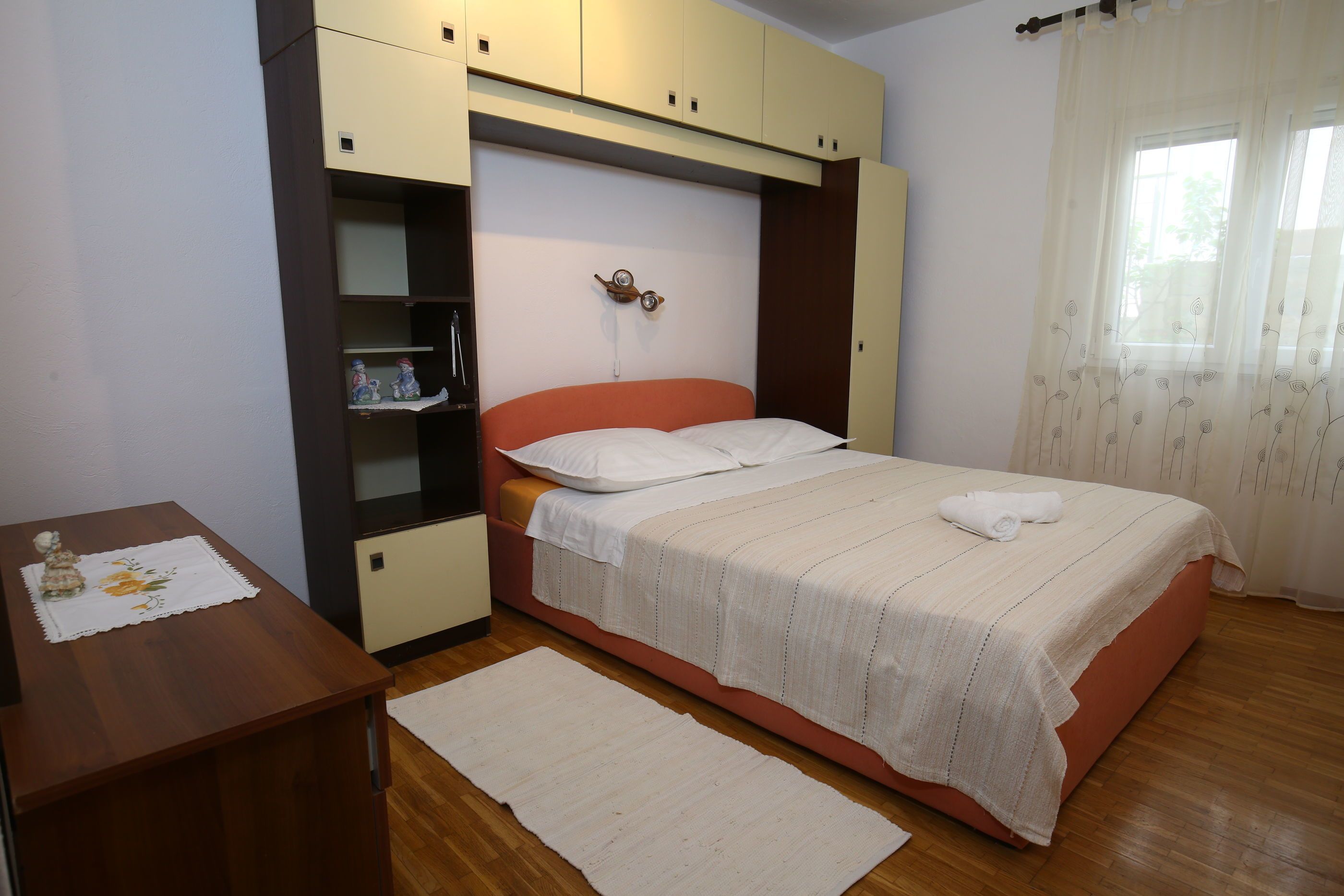 A bedroom with a bed, a desk, a shelf, and a window with curtains.