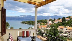 A balcony with a table and chairs, overlooking a lake and town. - Apartments Boro (Splitska)