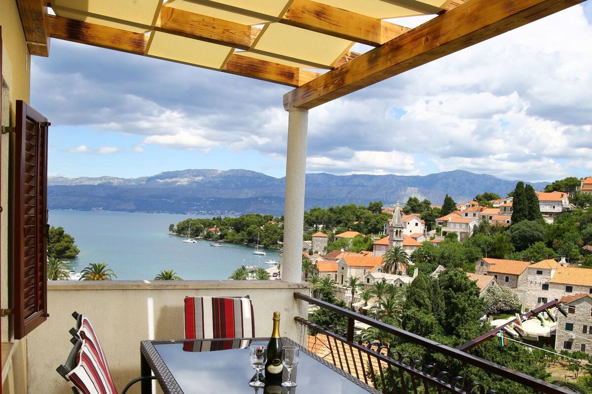 Ein Balkon mit Tisch und Stühlen mit Blick auf einen See und ein Dorf.