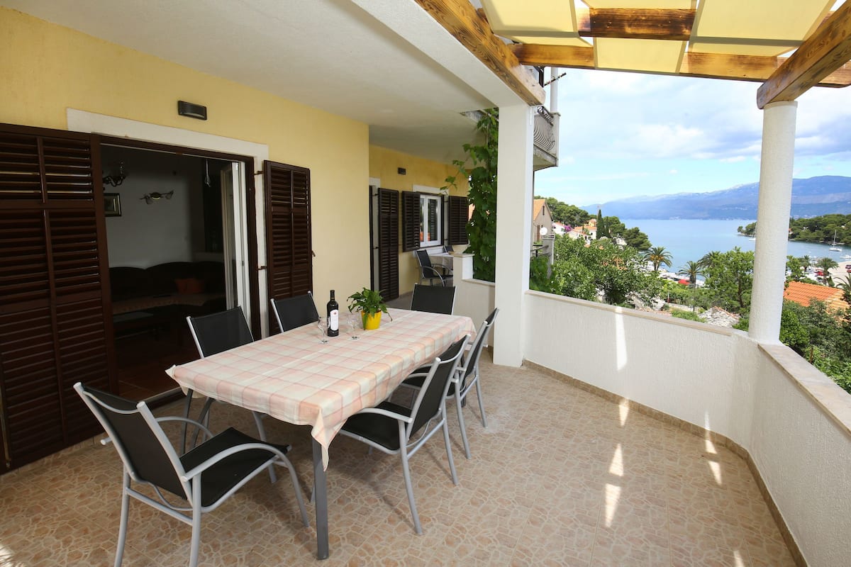 Ein Balkon mit Tisch und Stühlen, Blick aufs Meer, und ein Gebäude mit gelber Wand und Holzläden.