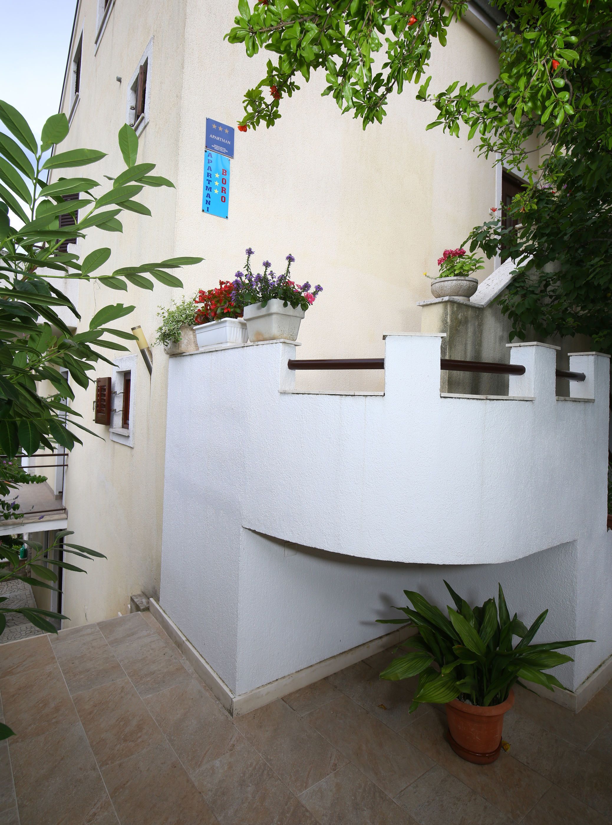 Un edificio blanco con balcón, plantas en macetas y un letrero azul.