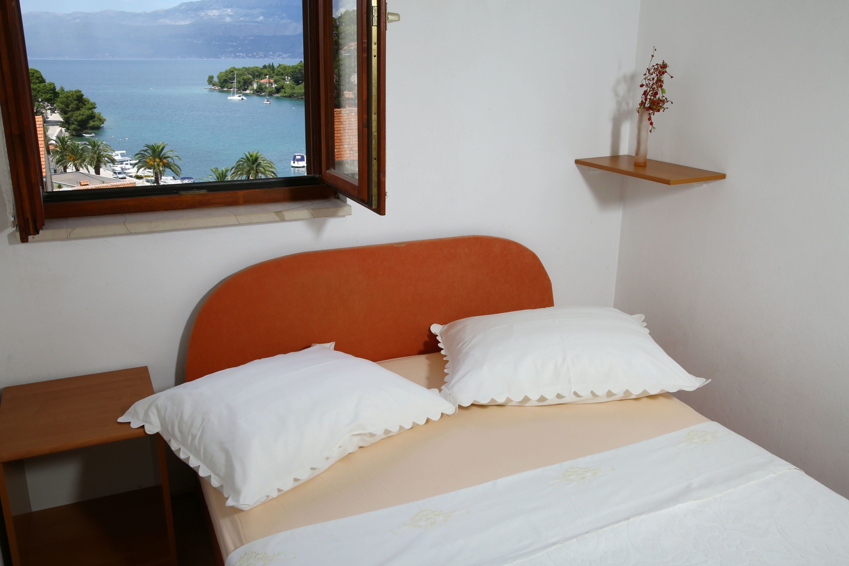 Une chambre à coucher avec un lit, une fenêtre donnant sur la mer et une petite étagère avec une plante.