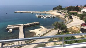 A coastal marina with boats docked, a clear blue sea, and a road leading to a residential area with houses and greenery. - Apartments Suzana (Jakisnica)