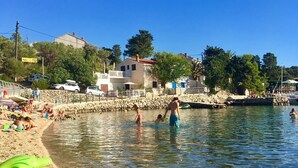 A beach with clear water, people swimming, and a lifebuoy on the sand. - Apartments Suzana (Jakisnica)