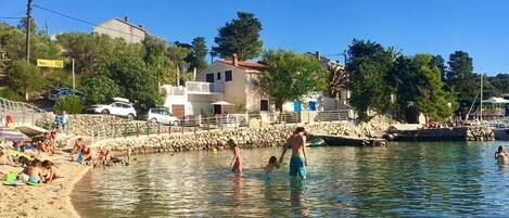 A beach with clear water, people swimming, and a lifebuoy on the sand.
