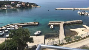 A coastal marina with boats docked, a clear blue sea, and buildings in the background. - Apartments Suzana (Jakisnica)