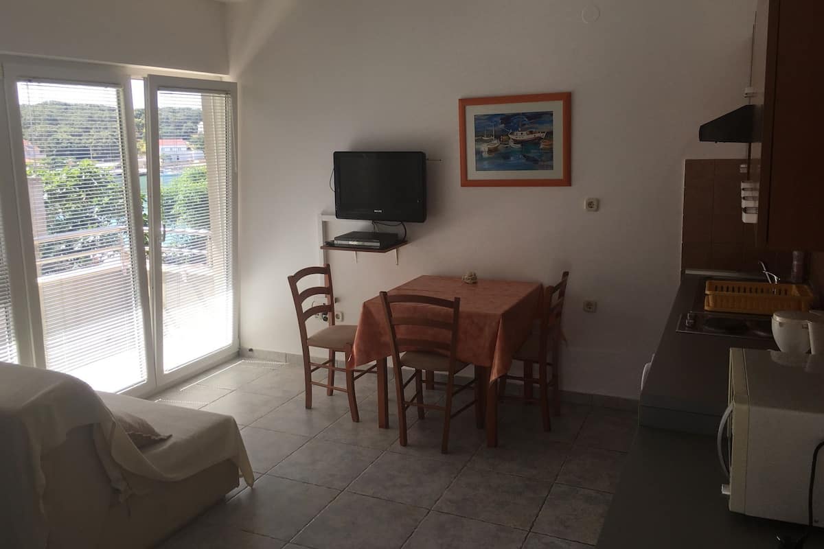 A dining area with a table and chairs, a television on a shelf, and a painting on the wall.