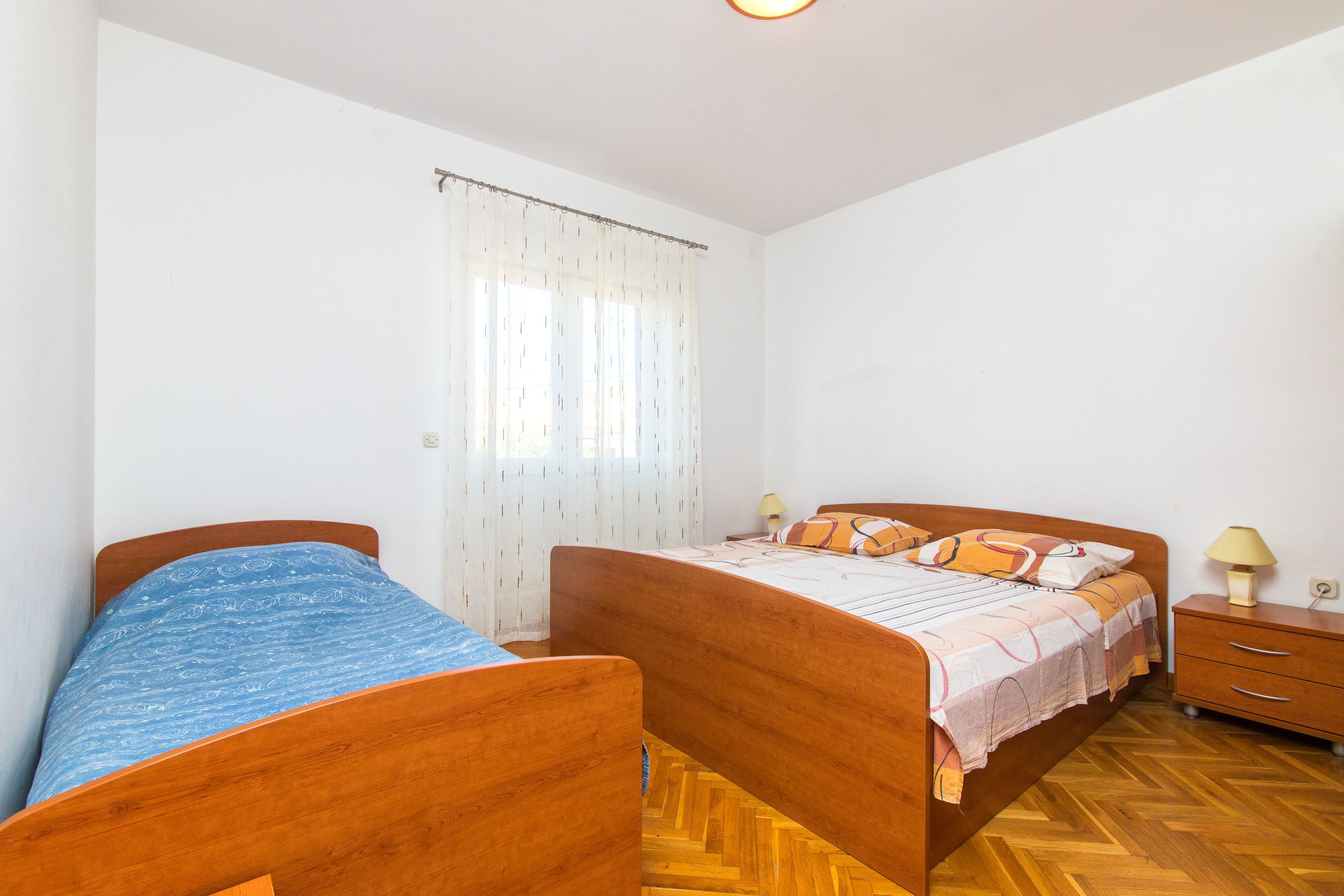 A bedroom with two wooden beds, a nightstand, a lamp, and a window with curtains.