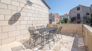 A patio with a table and chairs, a lamp, and a view of neighboring buildings. - Apartment Jerka (Supetar)