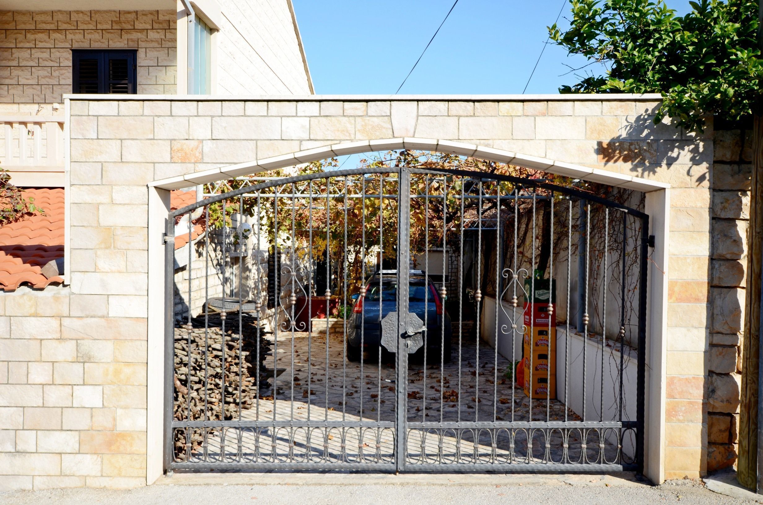 Uma entrada com portão, um carro estacionado no interior, um muro de pedra e uma árvore com folhas de outono.