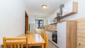 A compact kitchen with a wooden dining table, white cabinets, and a built-in oven. - Apartment Jerka (Supetar)
